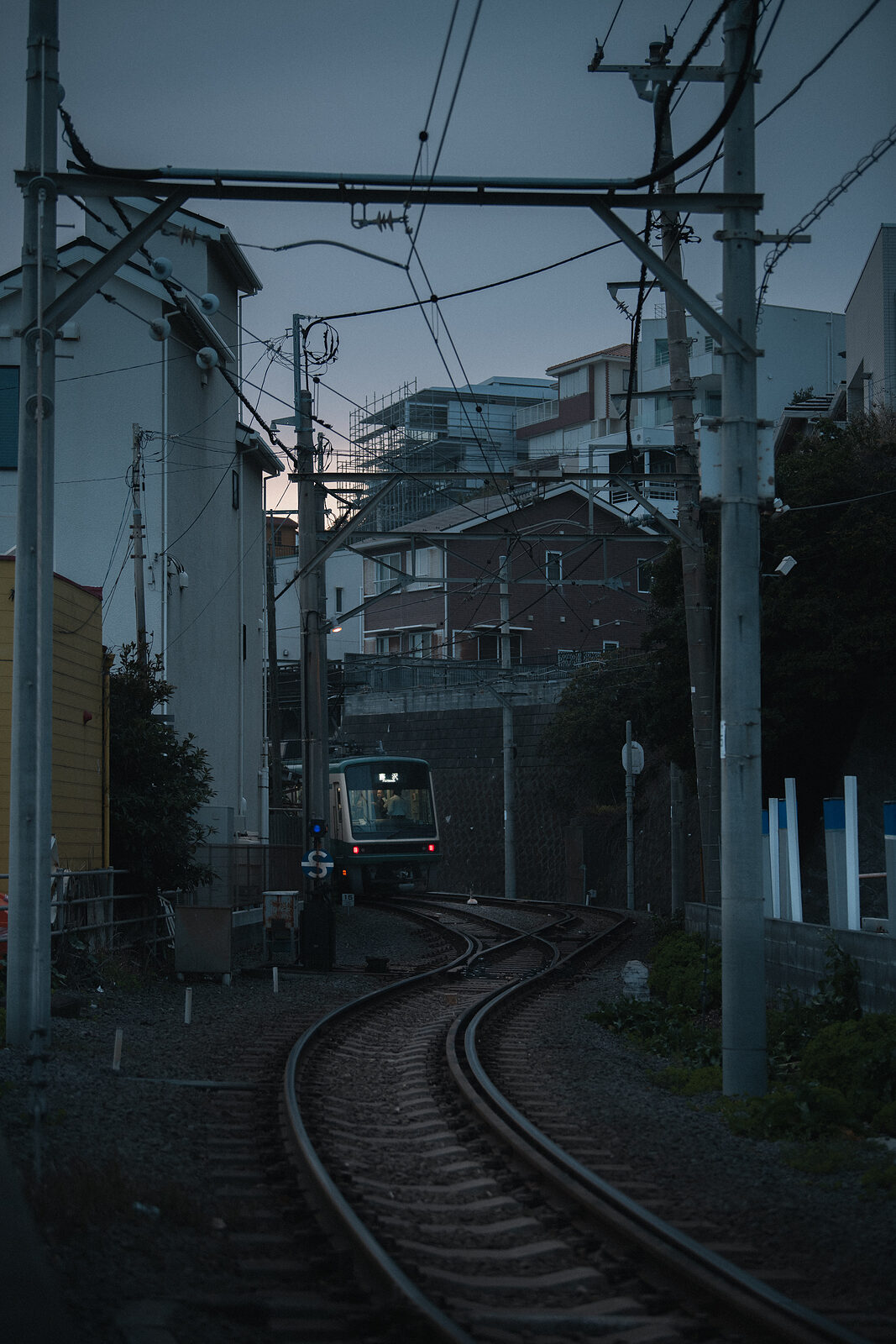 A train approaching along curving tracks through residential houses at evening