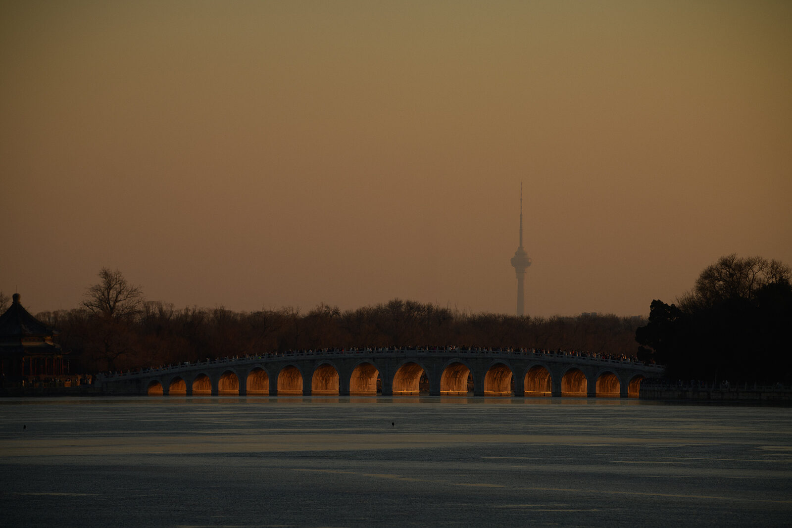 The Seventeen-Arch Bridge glowing gold beneath its arches at sunset, a distant tower fading into haze